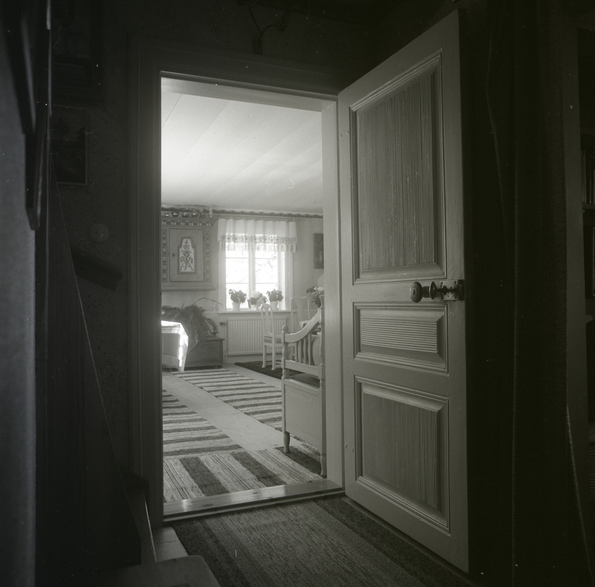 En öppen dörr leder till ett rum med bland annat väggskåp, kista och trasmattor.