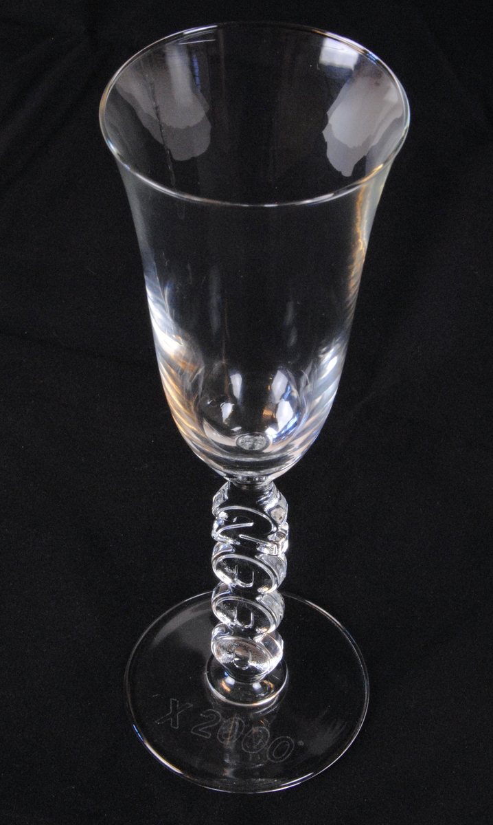 Två champagneglas av pressglas i flûtemodell med tulpanformad kupa. Stjälken är utgörs av texten "2000" med siffrorna staplade på varandra. Foten är cirkelformad och har texten "X 2000" ingraverad i kursiv.

Jvm23606:1 och :2 är identiska.