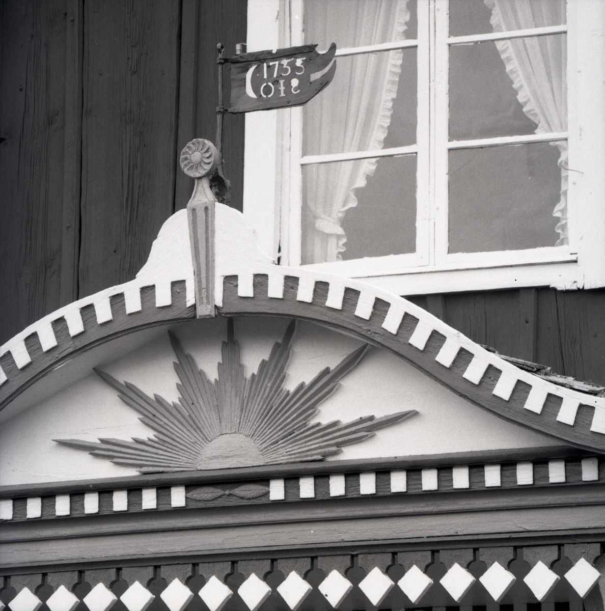 Ett dekorerat överstycke till en förstukvist på ett hus i Grängsbo. På nokspiran sitter en vindflöjel märkt med ett årtal.