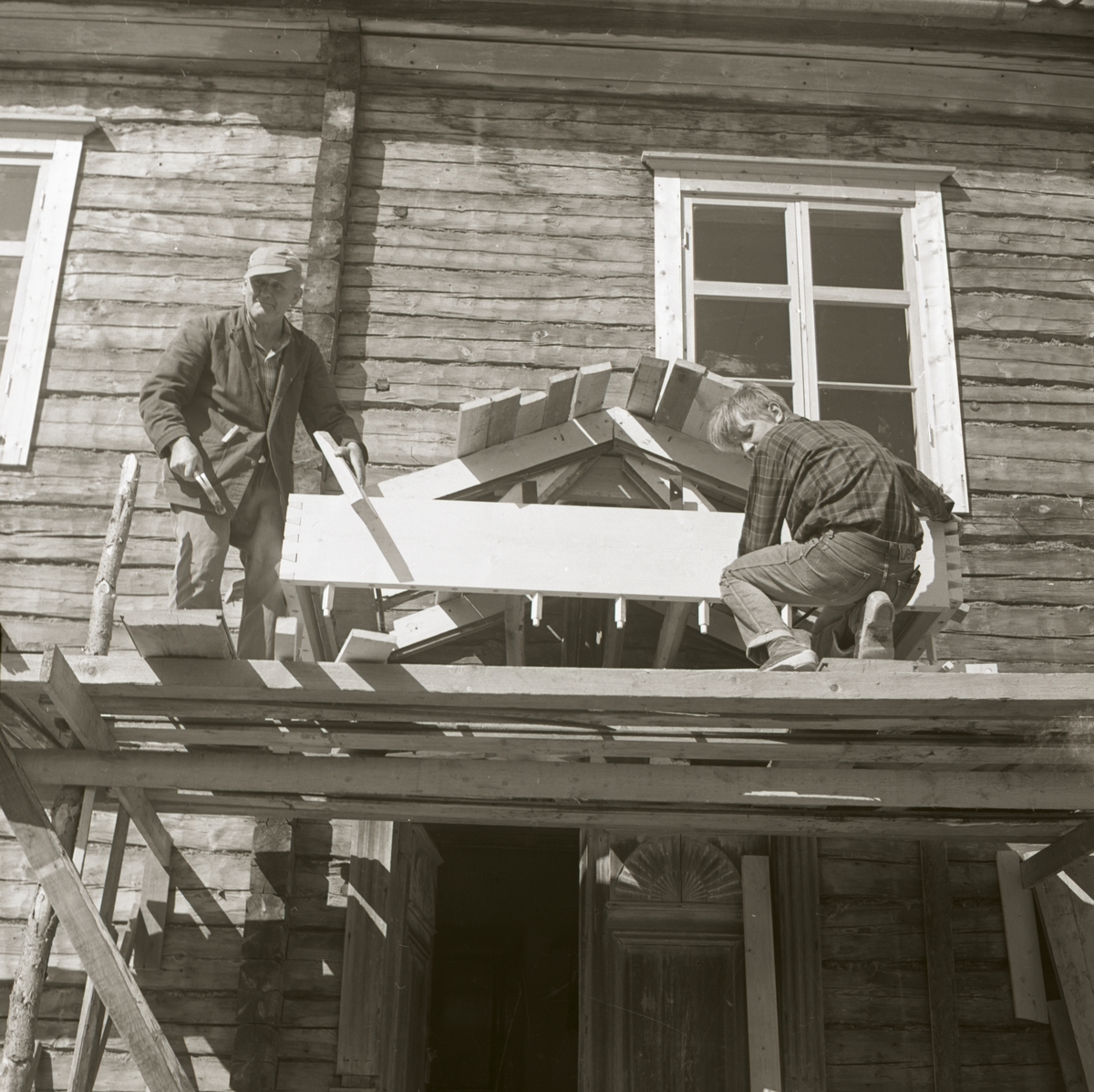 Två män står på en byggställning intill en nygjord förstukvist vid Norrgården, 1968 i Rengsjö.