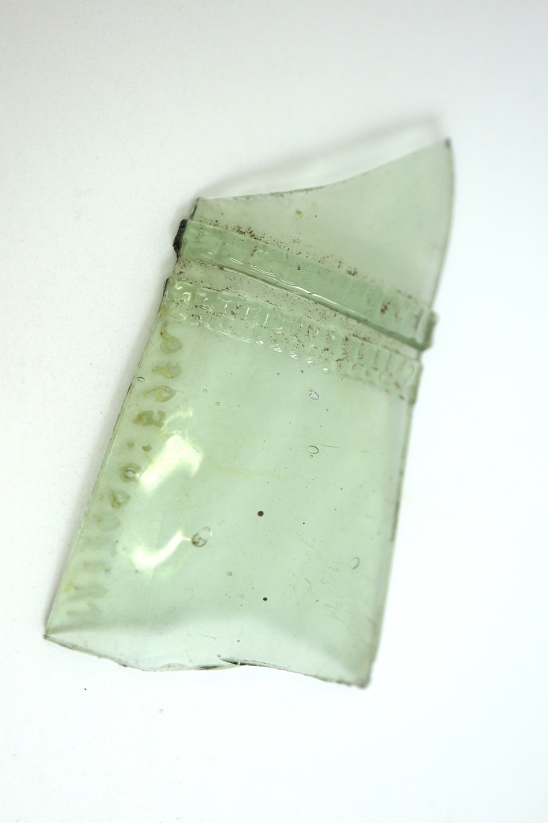 Två sammanhörande fragment av ett kägelformat passglas av gröntonad glasmassa. Pålagda strierade trådar.