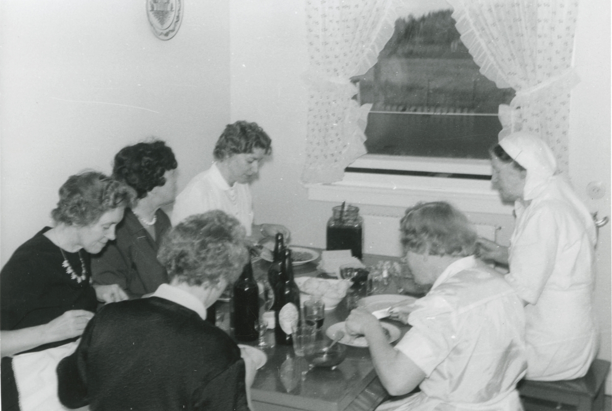 Flere damer sitter rundt kjøkkenbordet og spiser.
