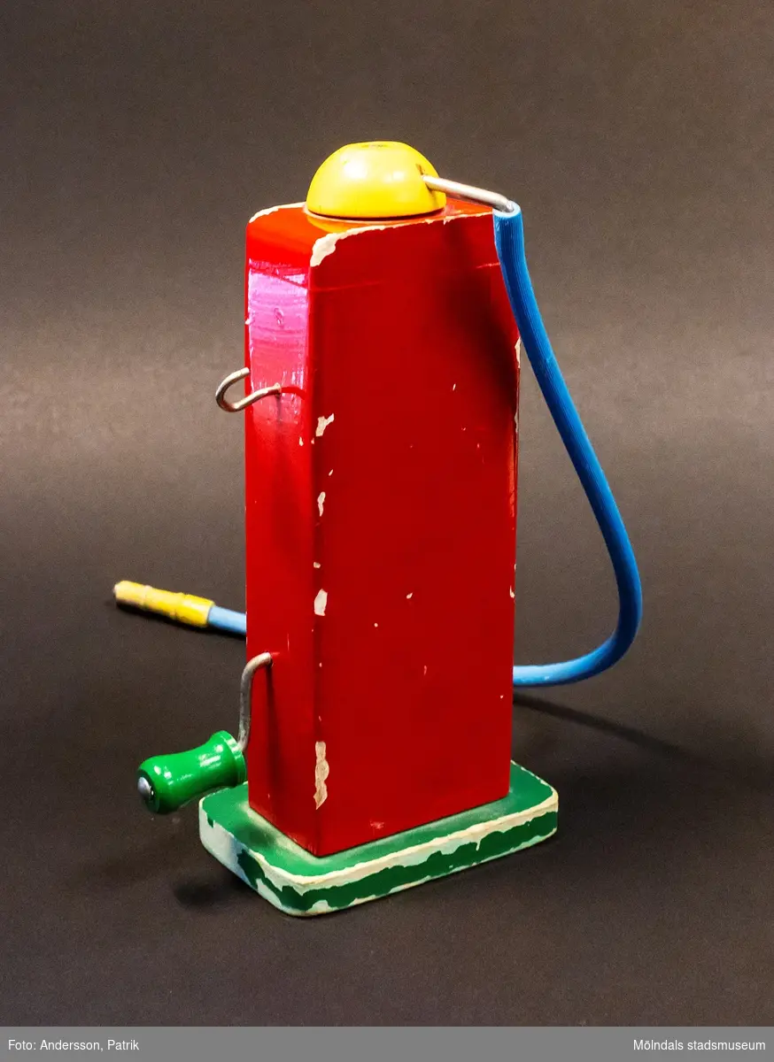 Esso bensinpump i trä. Något sliten. Pumpen är röd och står på en grön platta. Överst på pumpen sitter en gul roterbar knapp och från den löper en blå gummi-slang att tanka med. Fronten är vit och på den nedre delen ses Esso-logon (blå-vit-röd) och på ovandelen ses en blåmålad liter-ruta (0 - 90 liter) med en gul visare i mitten. Visaren är sammankopplad med en vev som sitter på pumpens högra sida i höjd med Esso-logon och som går att snurra på. Ovanför veven sitter en krok att hänga gummi-slangen på. Tillverkad av Brio. Inköpt av givaren år 1970 i Mölndals leksaksaffär på Kungsbackavägen och användes av sönerna Anders (född 1970) och Mathias (född 1973).