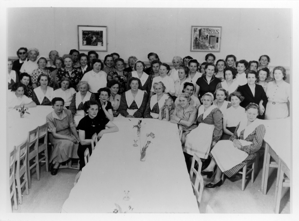 Gruppbild av omkring 60 kvinnor, stående samt sittande, från Alingsås Kooperativa Kvinnogille under deras 25-års jubileum. Vid mitten bordet ses även en flicka.