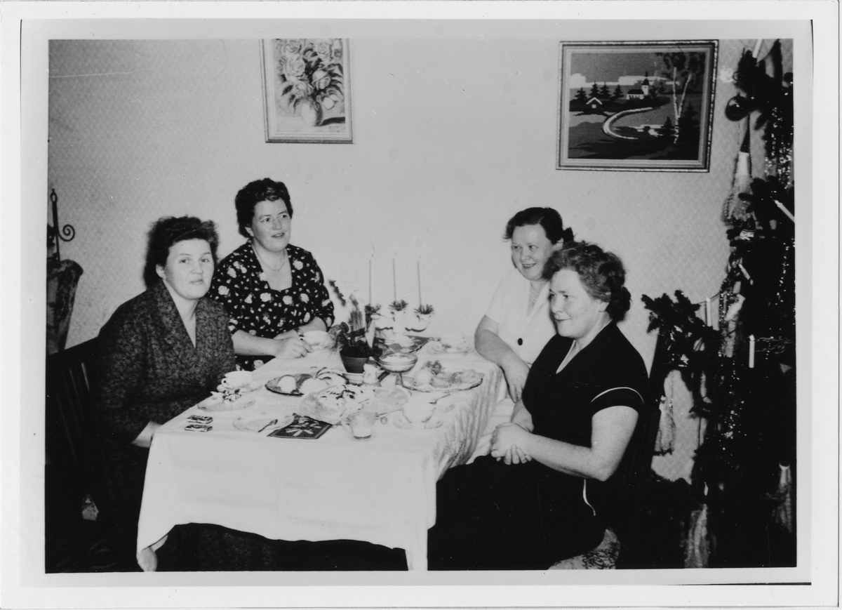Fyra kvinnor, bland annat Inez Jansson, vid ett uppdukat julbord med kaffe och kaka. Till höger på bilden ses en pyntad julgran och på väggen två tavlor.