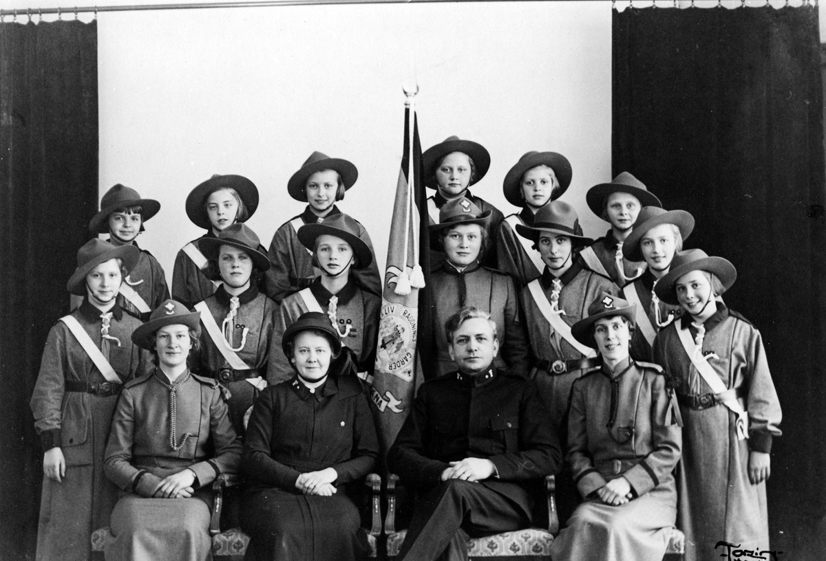 Gruppbild med 13 flickor, 3 kvinnor och 1 man klädda i Frälsningarméns Livräddninggardes uniform.