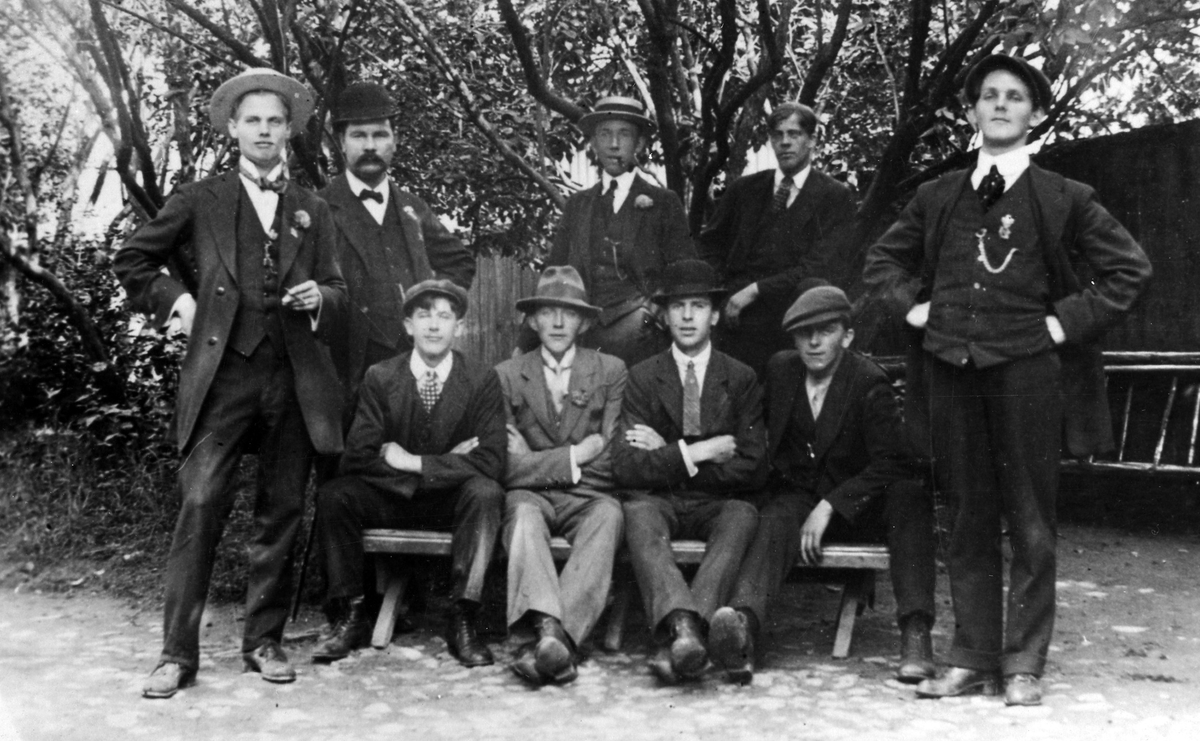 Gruppbild på en samling Alingsåsare omkring 1900. Gruppeb består av nio män som samlat vid en parkbänk.