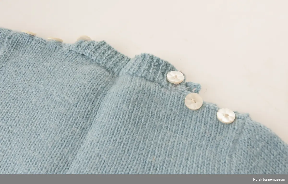 Blå strikkegenser til barn, med hvite striper og knappelukning på skulder.