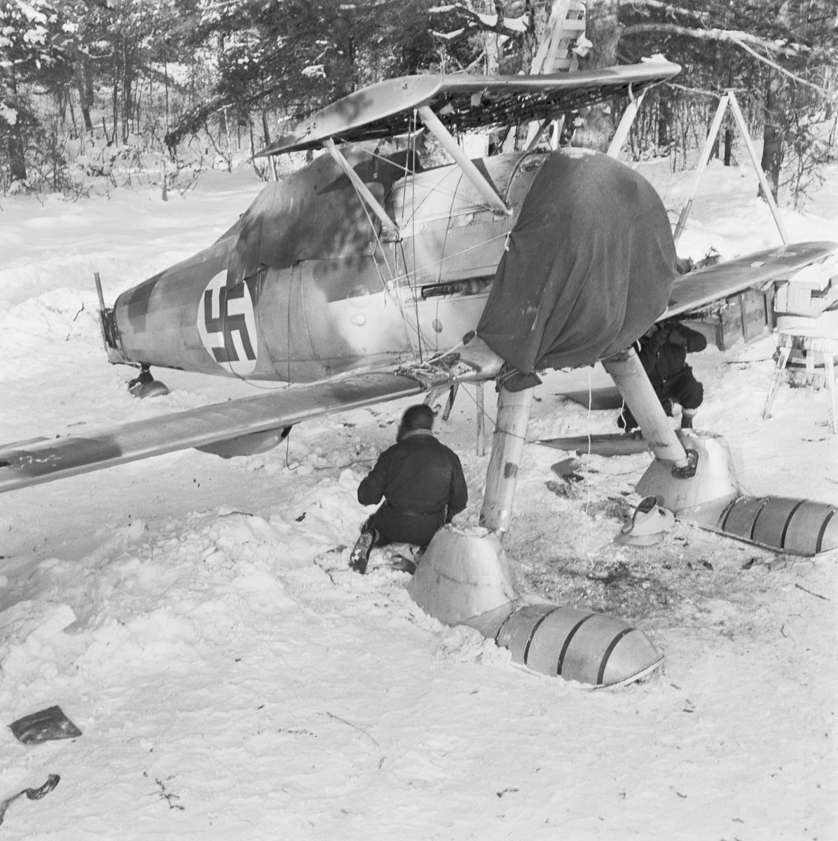 Demontering av flygplan Gloster Gladiator efter Finska vinterkrigets slut i mitten av mars 1940 vid Svenska frivilligkåren i Finland, F 19. Två militärer i arbete under flygplanets vingar.
