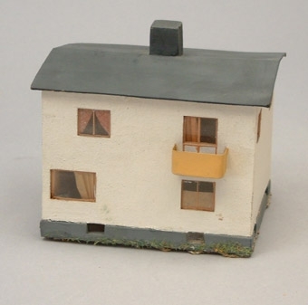 Modell i skala 1:87 av vitt tvåvånings bostadshus med gul balkong och grått tak.