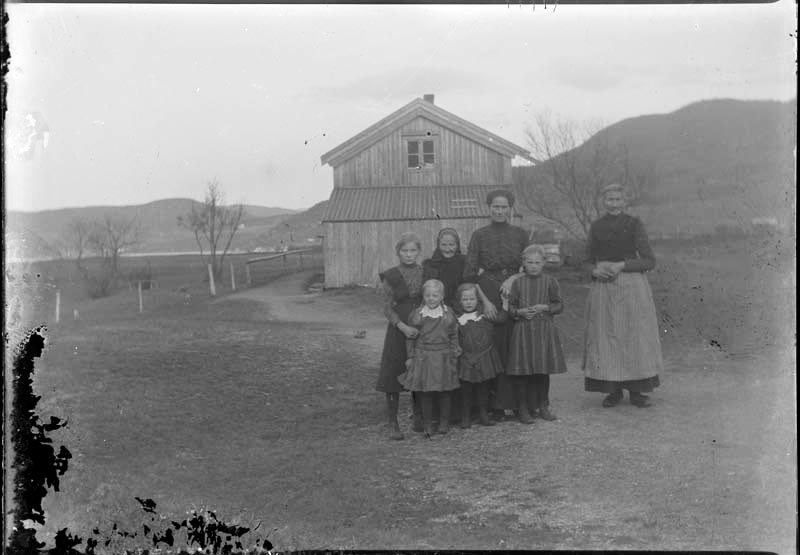 Fire jenter og tre voksne kvinner, utenfor på Dolstadsjøen med huset i bakgrunnen.