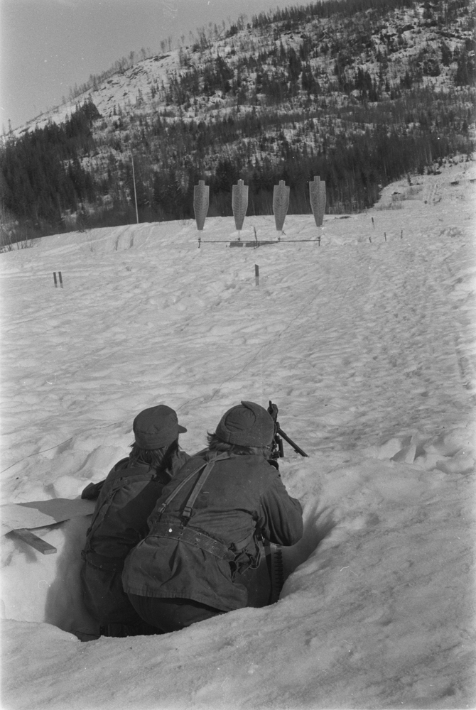 Repetisjonsøvelse på Drevjamoen. 
2 soldater i skyttergrav på skytterfelt som skyter mot silhuetter med maskingevær.
