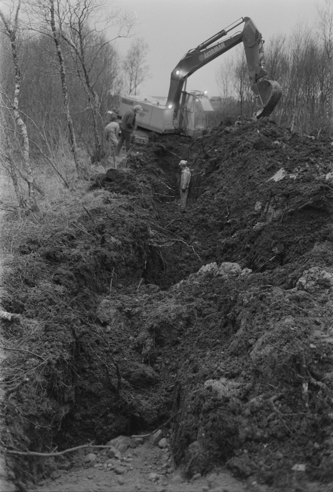 Legging av vannledning til Søvik. Gravemaskin som graver grøft og personer.