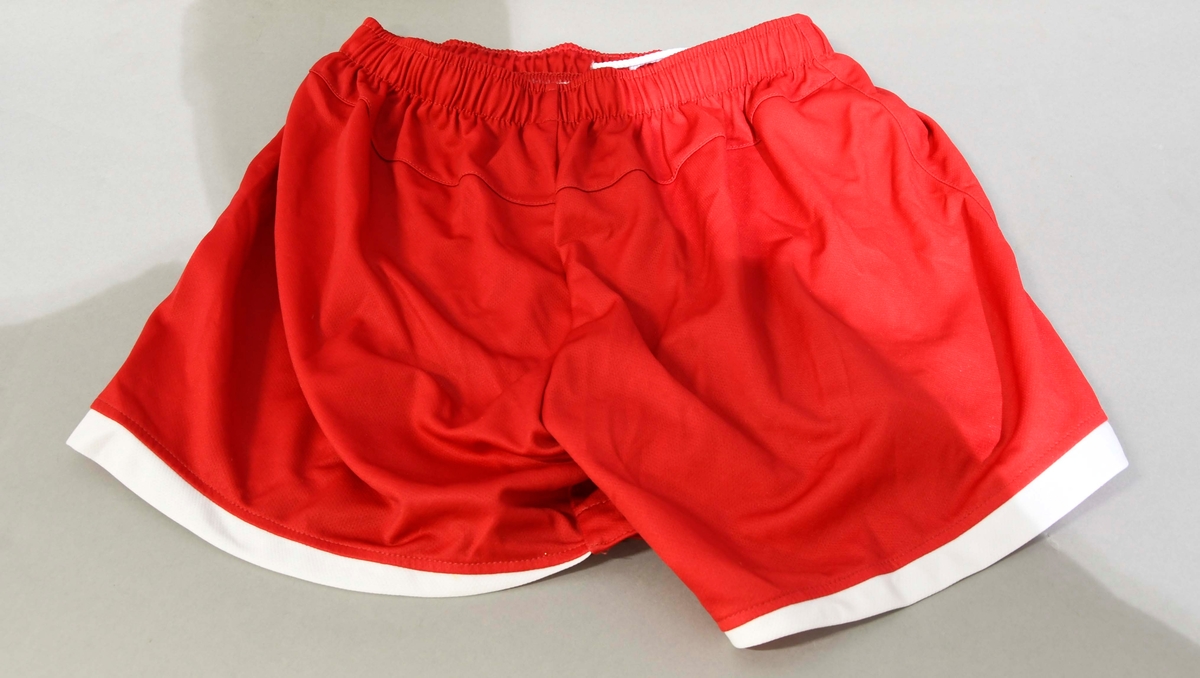 Rød shorts med hvite kanter, strikk i livet.Str.:38
Umbros logo brodert foran på høyre ben.