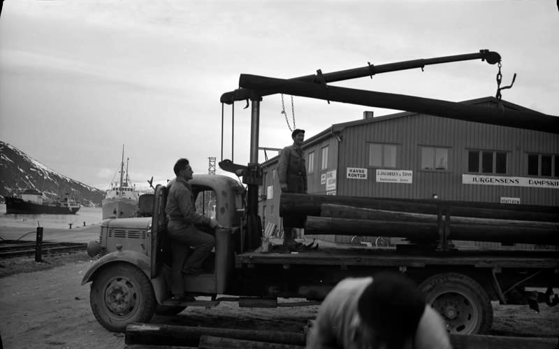 Folk fra Helgeland Kraftlag laster stolper på Jernbanekaia, med en lastebil (Bedford O-serie, prod. 1946-53).
