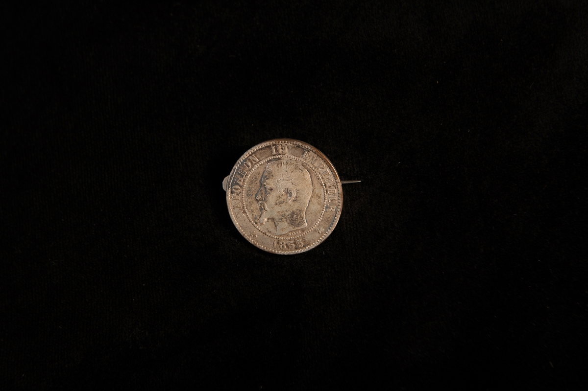 En rund brosch av silver i form av franskt mynt (10 centimes) från 1855.