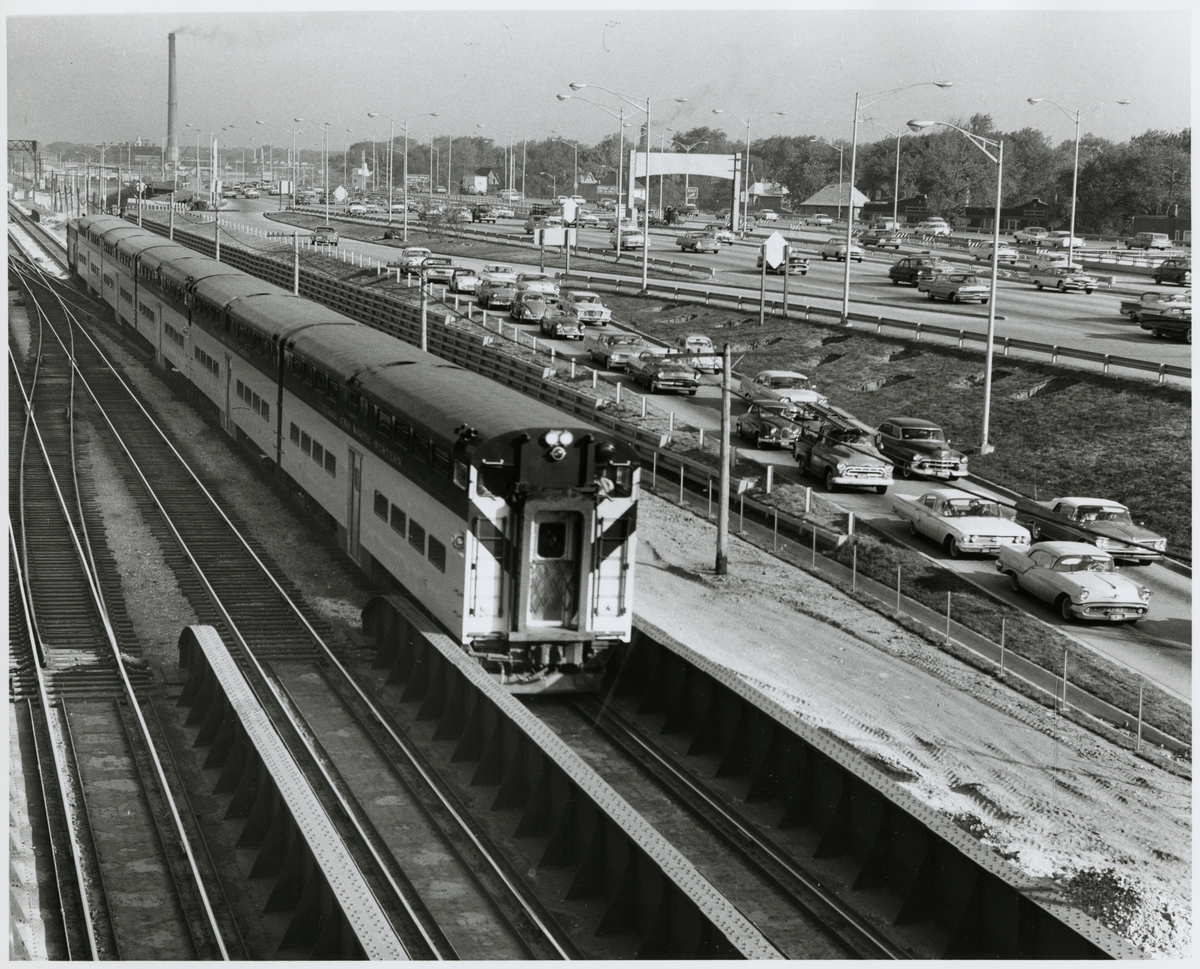 Ett Chicago and North Western Railway, CNW persontåg bredvid en större motorväg.