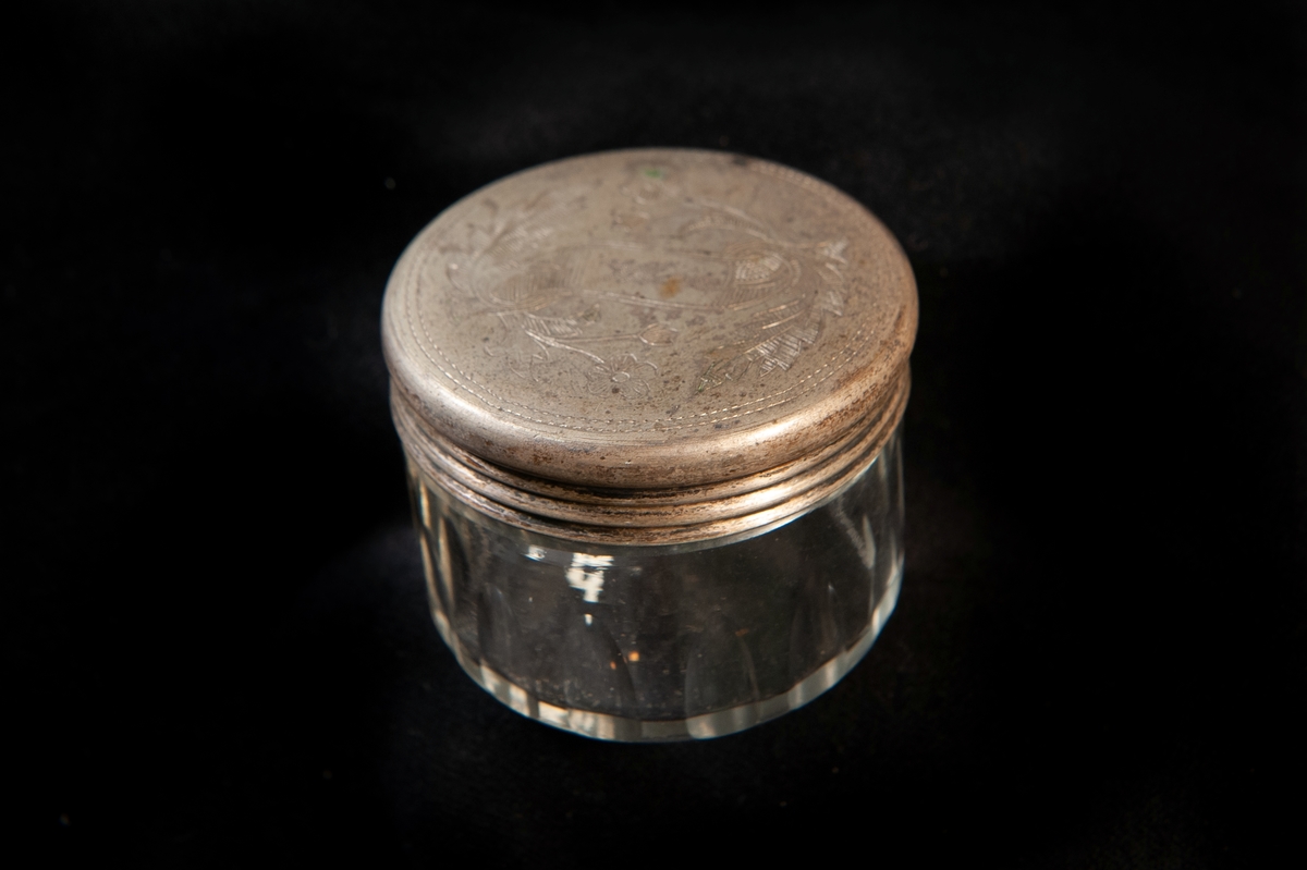 Rund dosa i olivslipat glas. Runt lock av metall, graverat med blomslingor och namn: "Wivi" på ett band. Locket troligen gjort av nickel eller nysilver. Ostämplat.