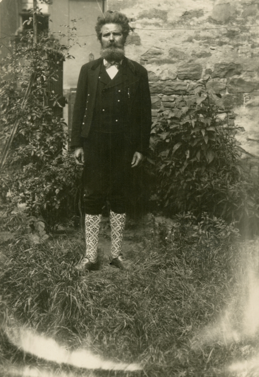 Portrettfotografi av Ingvald Skjeldrup kledd i bunad i hagen foran et hus.