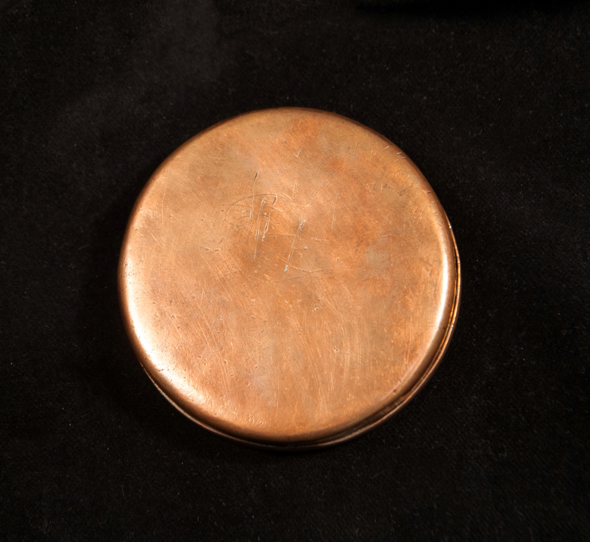 En rund tobaksdosa av koppar. På locket (otydlig) punktgravyr: "Ao 1720, ASJL ".