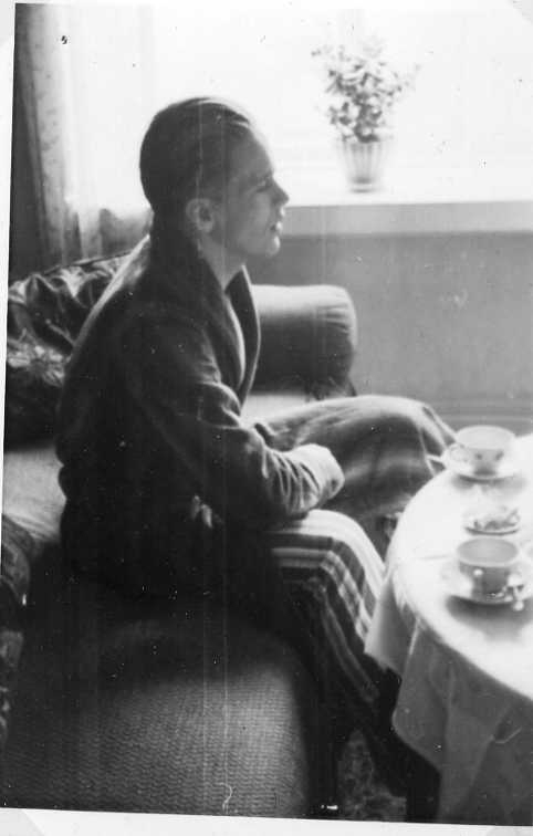 En man i profil sittande på en soffa i vad som ser ut att vara pyjamasbyxor och morgonrock. Framför honom ett runt bord med duk och två kaffekoppar och ett askfat.