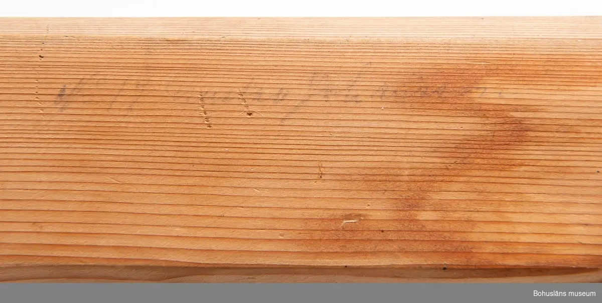 Bräda med två öglor av järn för upphängning samt två skurna träpinnar infällda i borrhålen. 
På framsidan texten: "N:19 Gustav Johansson".