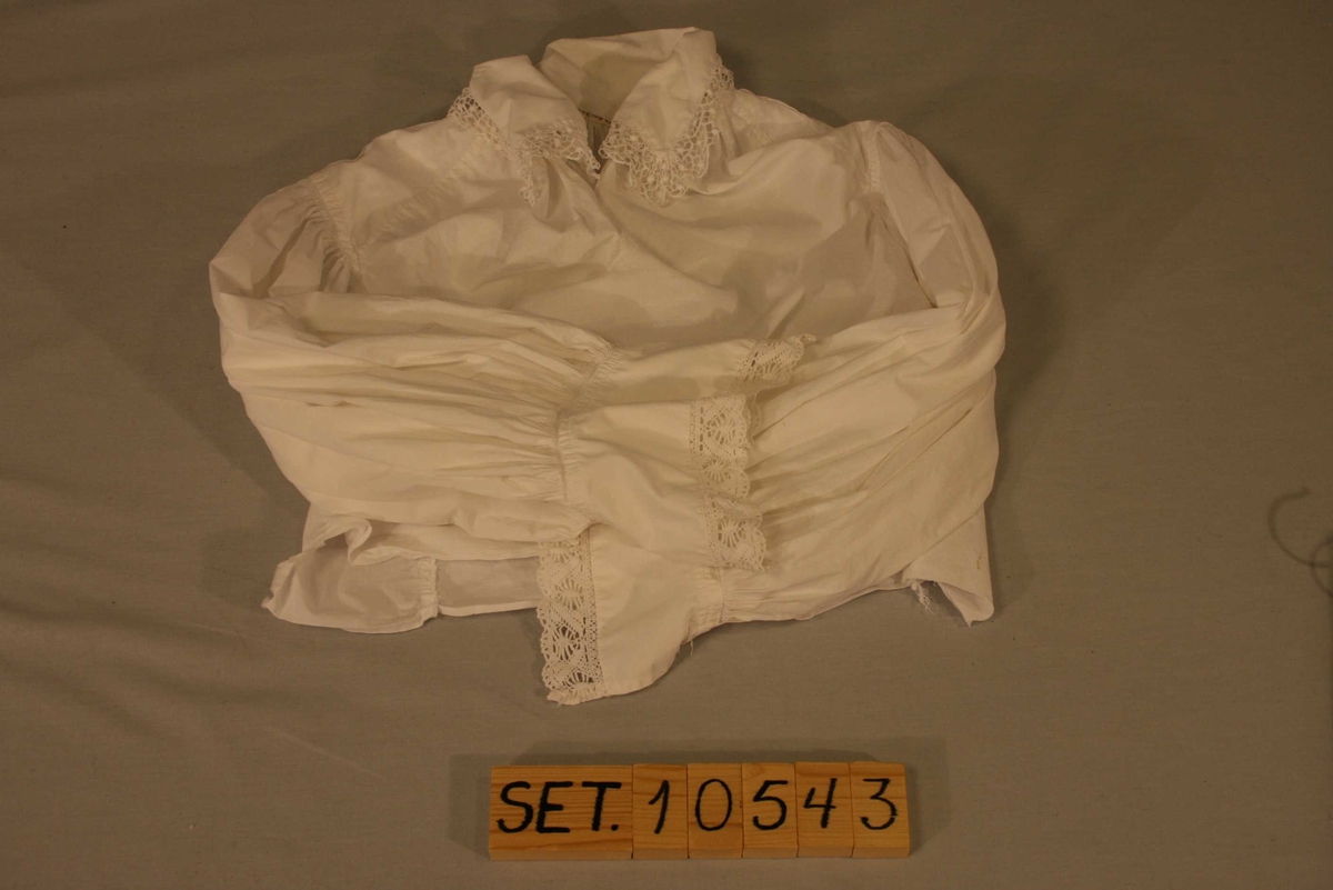 Kvit bomulsskjorte med lange ermar, blonder på krage og mansjettar.