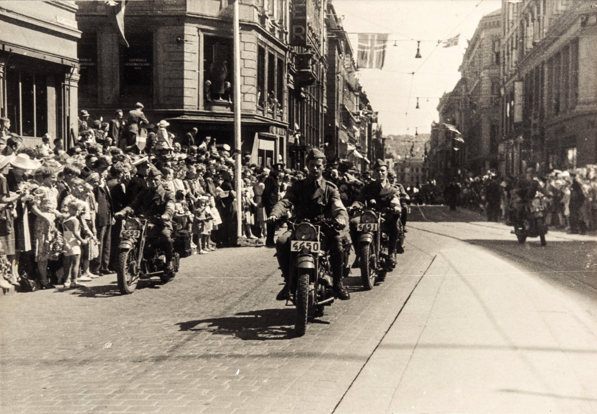 De norske polititropper (Feltbataljon IV) med motorsykler på vei opp Karl Johans gate i Oslo våren 1945. Store folkemengder hilser dem velkommen.