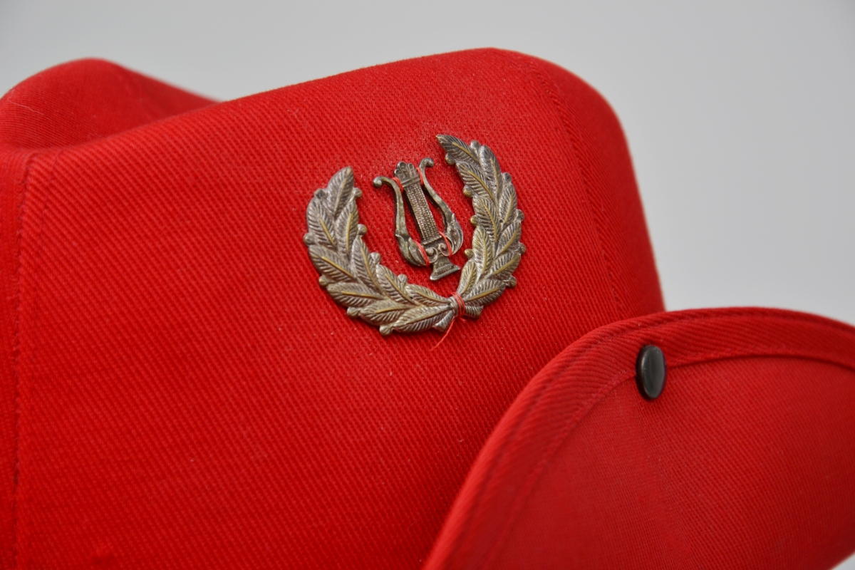 Rød uniformshatt med snor. Bremmen er festet til pullen.