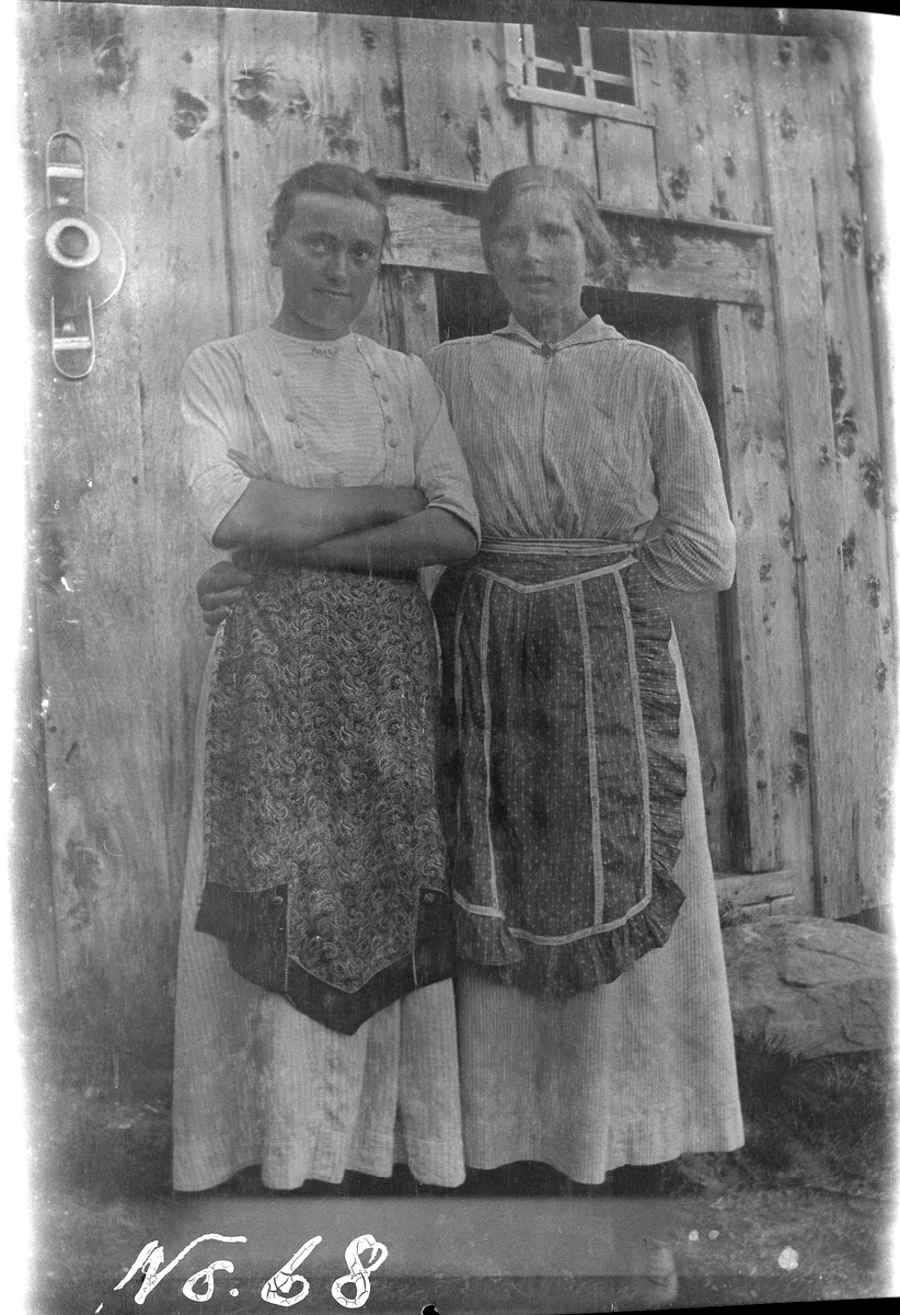 Portrett av to kvinner stående utendørs. Bygning i bakgrunnen.