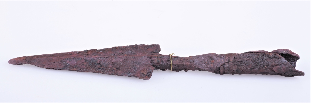 Spydspiss av jern, ganske som type Rygh 202 med 2 mothaker, beskadiget, fra yngre romersk jernalder. Funnet i en gravhaug på Sukkestad i 1888.
