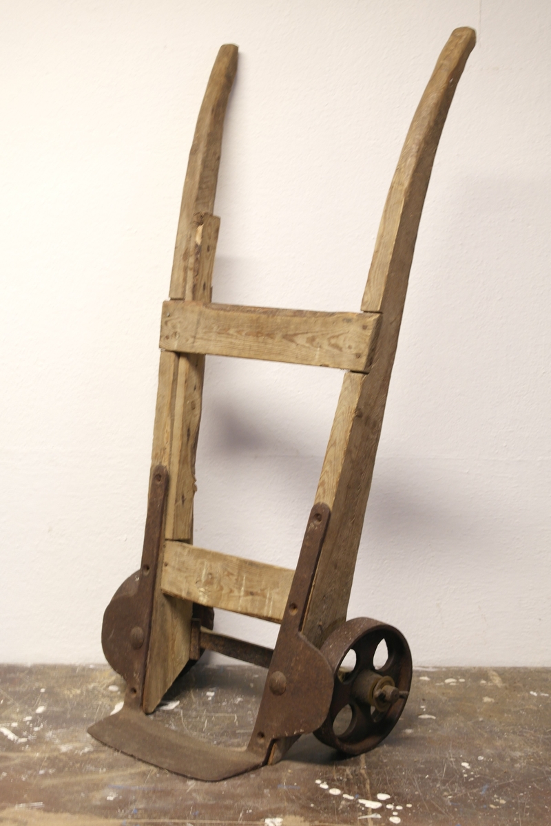Tohjulstralle med håndtak i tre og hjul og løftegaffel i jern.