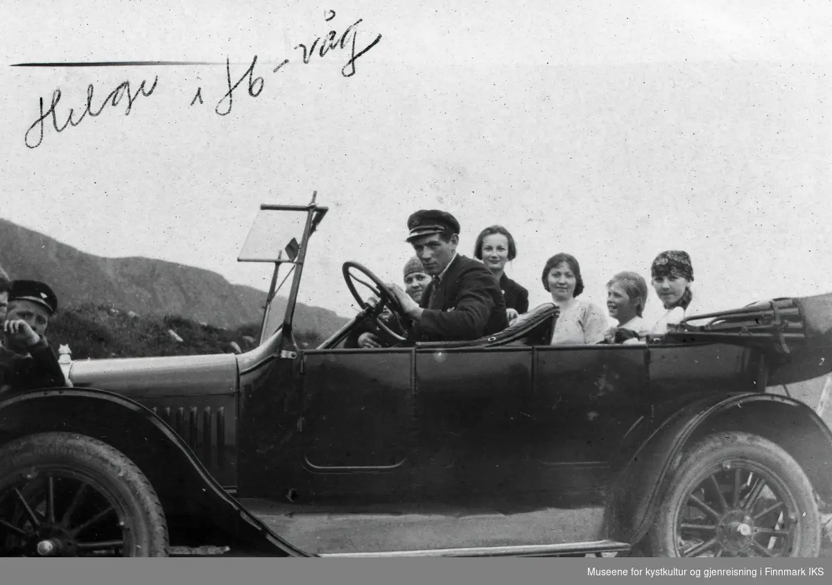 Honningsvåg. Drosjeeier Helge Helgesen med flere i åpen bil. På venstre siden står flere personer. 1930-tallet.