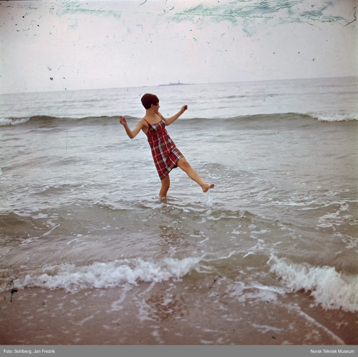 En kvinnelig modell ikledd strandkjole vasser i sjøen.