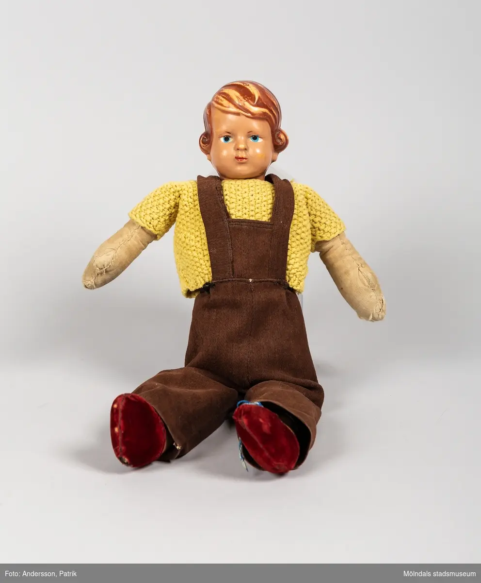 En docka som kallades Lill-Pelle. Dockan är från början av 1950-talet.
Rolf som bodde på en lantgård utanför Trelleborg, fick dockan när han var cirka 3-5 år. Dockans kropp och kläder är handsydda av hans moster Elsa som var född 1921. Lill-Pelles gula tröja är stickad av Rolfs syster Gun född 1947, då hon var i 10-årsåldern.