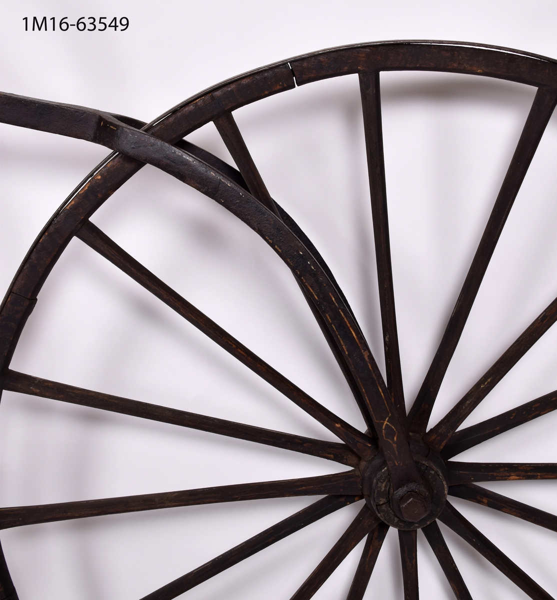 Cykel, gammal typ med högt framhjul. Tramporna är gjorda av trekantiga träbitar. Sadel av metall.