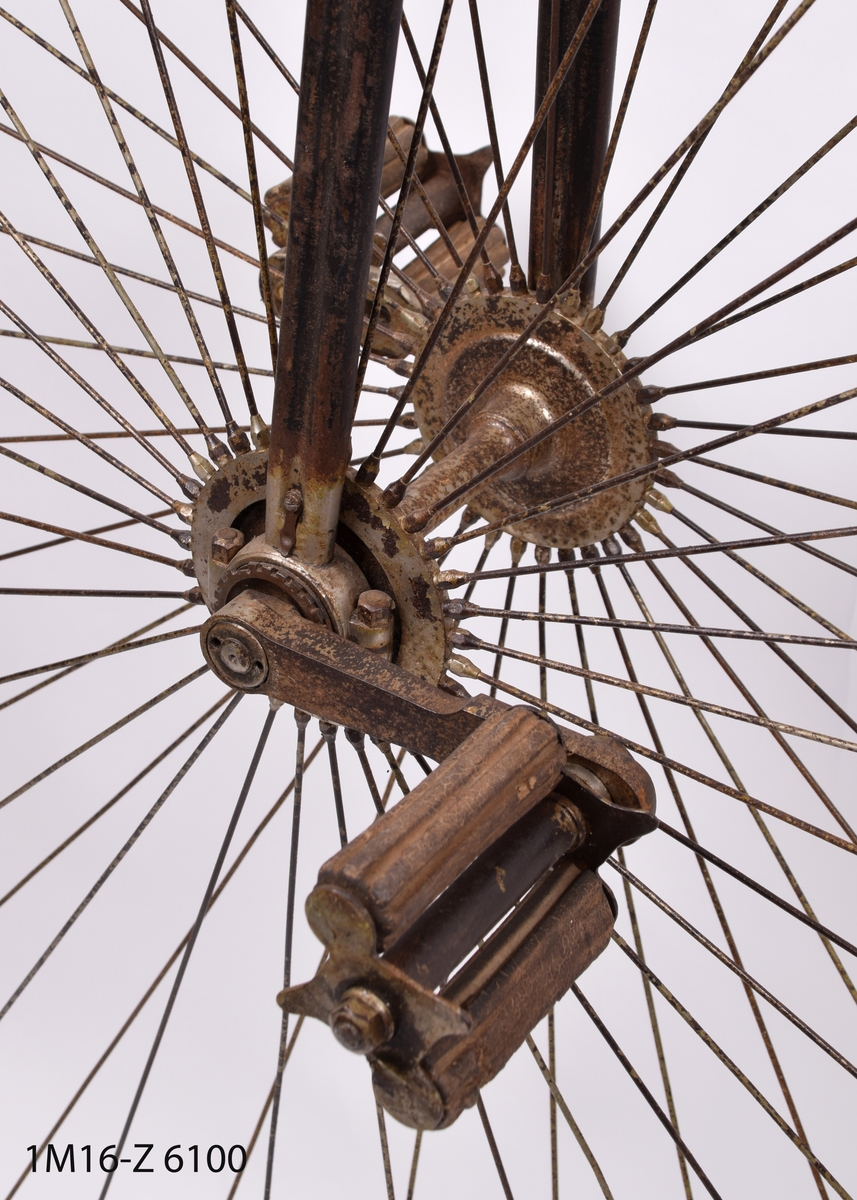Cykel, högvelociped, med mycket stor framhjul och litet bakhjul. Trähandtag på styret. Sadeln överdragen med läder.