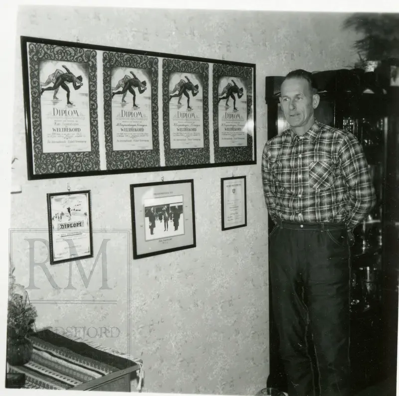Hans Engnestangen stående ved en vegg med noen av hans diplomer fra skøytekarrieren.