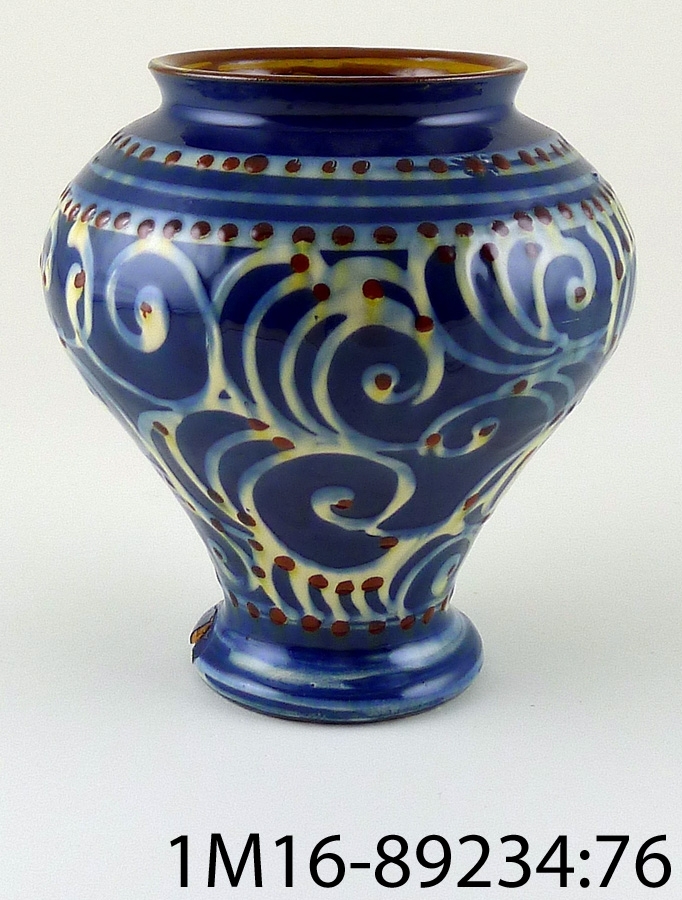 Urna av keramik, rund med blå brun och gulvit handmålad dekor. Märkt HK (Danmark).