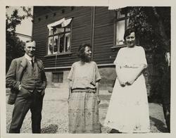 En mann og to kvinner står på gårdsplass foran bolighus i Sk