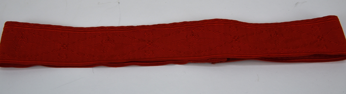 Ett mössband av rött mönstervävt tyg som fästs med kardborreband. Mönstret består av SJ:s bevingade hjul samt SJ:s logotyp i upprepande mönster.