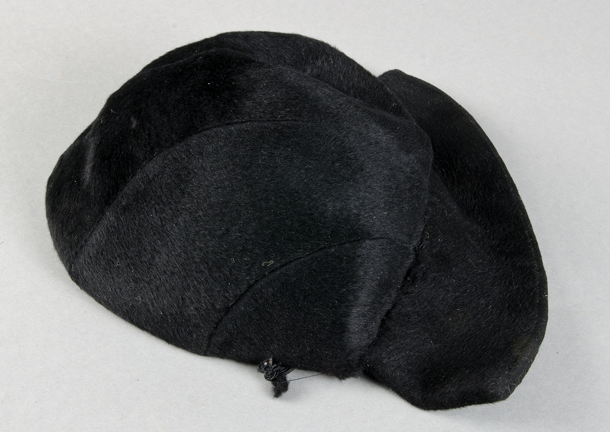Hatt av svart filt bestående av 6 st avlånga stycken som smalnar av vid nacken samt ett  7 cm brett nackstycke, svettband av svart rips, svart nacksnodd.
