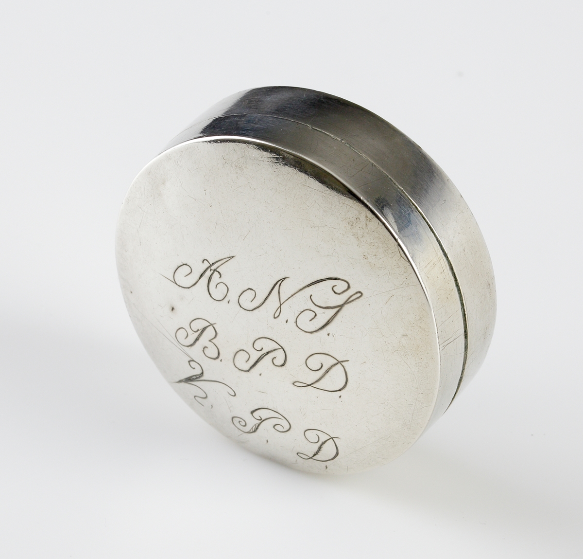 Dosa i silver.
Rund, slät modell med ägarinitialer: "A.N.S., B.P.D., K.P.D." på lockets ovansida. Stämplar på lockets insida.