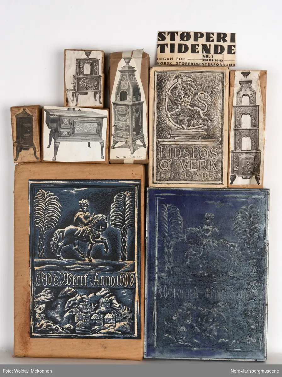 Klisjjer pakket inn i papir med motivbildet pålimt oppå motivene er diverse ovnsmodeller og illustrasjoner til Eidsfos Verks jubileumsskrift 1897.