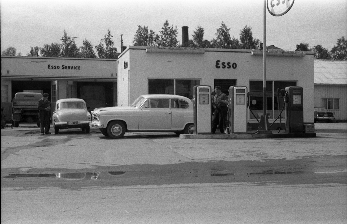 Esso bensinstasjon på Lena april 1958. Det står biler både ved pumpene og på vaskeplassen; en Wartburg med reg.nr. E-3085, og en Borgward Isabella ved pumpa. Personene er ikke identifisert. Bildet er tatt gjennom vinduet i Lena Foto & Radio i "Raubua".