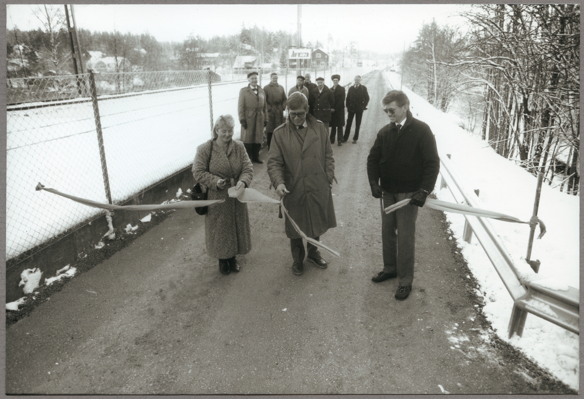 Representanter från kommunen och Trafikaktiebolaget Grängesberg - Oxelösunds Järnvägar, TGOJ inviger den nya vägen i Bälgviken den 1 december 1987. De som klipper invigningsbandet är, från vänster: Nina Jarlbäck, Jan-Erik Andersson och Bo Aldurén.