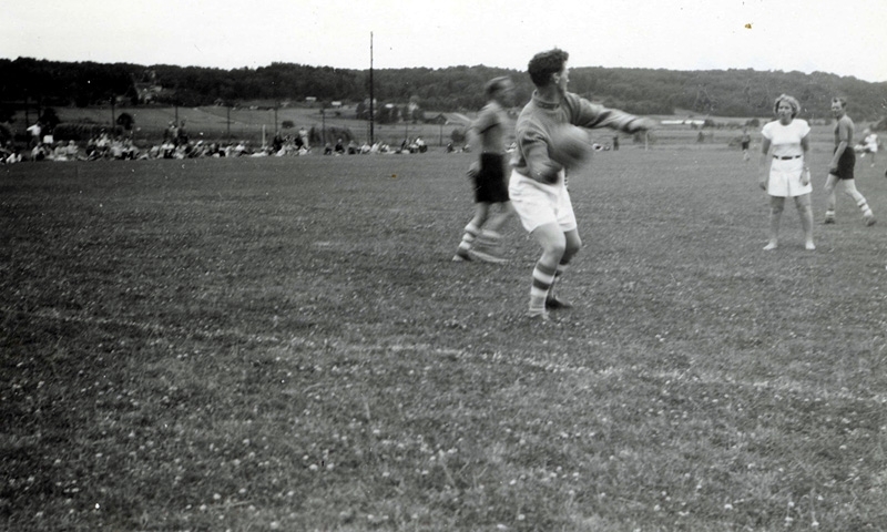 Kvinnor och män spelar fotboll på Kärret i Kållered år 1949. Det är invigning av fotbollsplanen. Detta är nedanför prästgården på Gamla Riksvägen. Coop hade senare sina p-platser på samma plats.