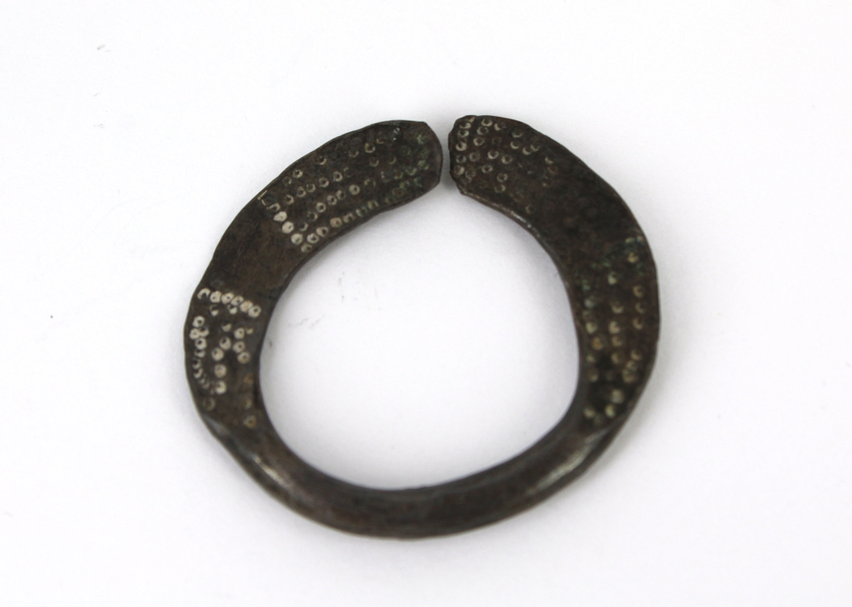 Metallringar av okänd användning, möjligen magiskt syfte. En platt ring med två fingerringar påträdda. Alla ringarna äro prydda med små punkter m.m. Diam. av den större ringen 3,3 cm. Dåligt arbete.