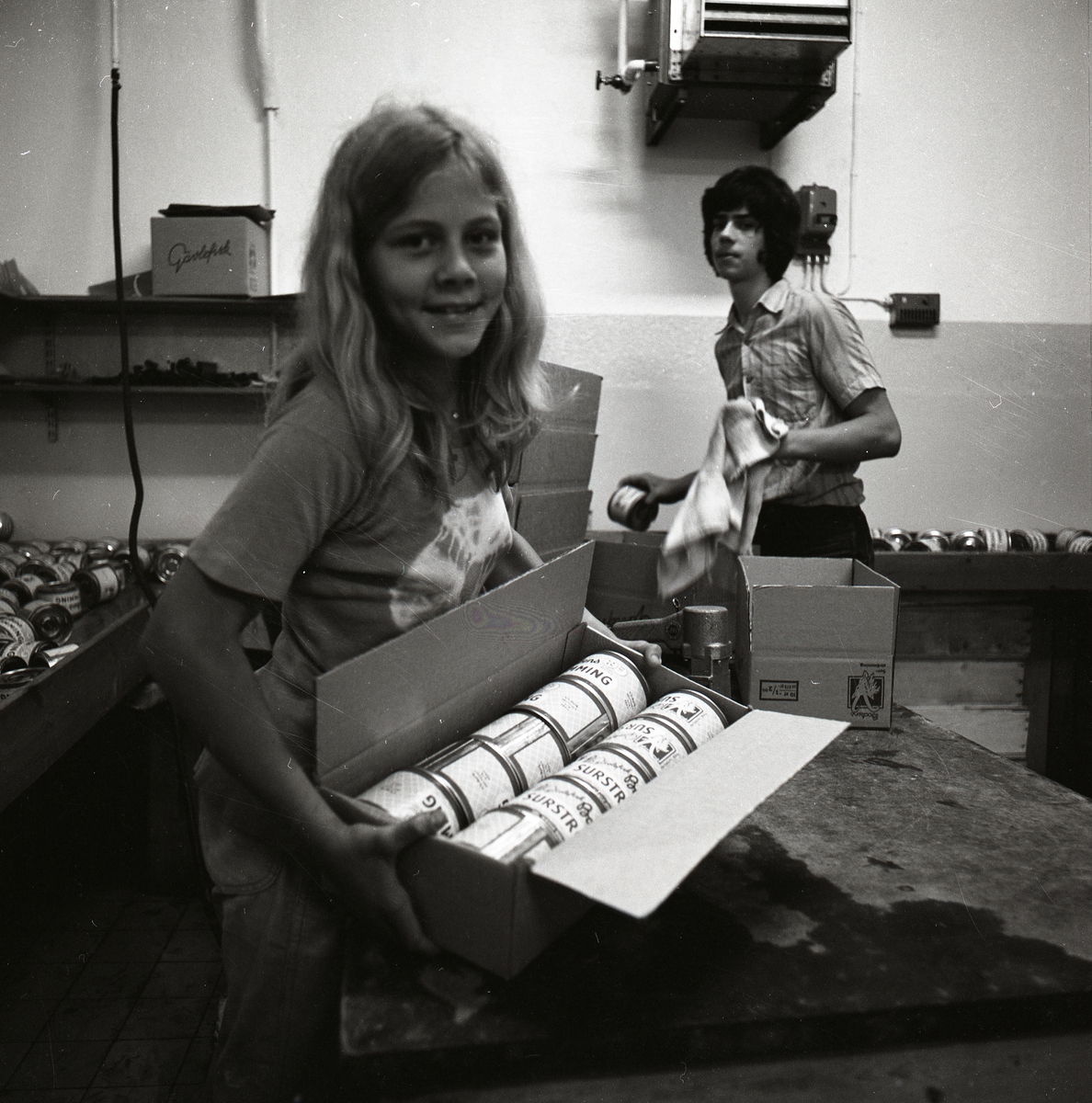 En flicka bär en låda med surströmmingsburkar.