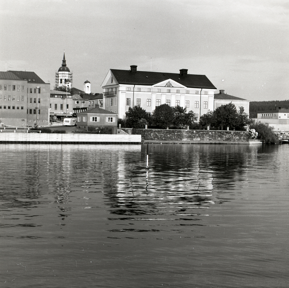 I bakgrunden skymtar tornet på Härnösands domkyrka fram och andra byggnader i staden speglas i vattenytan, Härnösand 1974.
